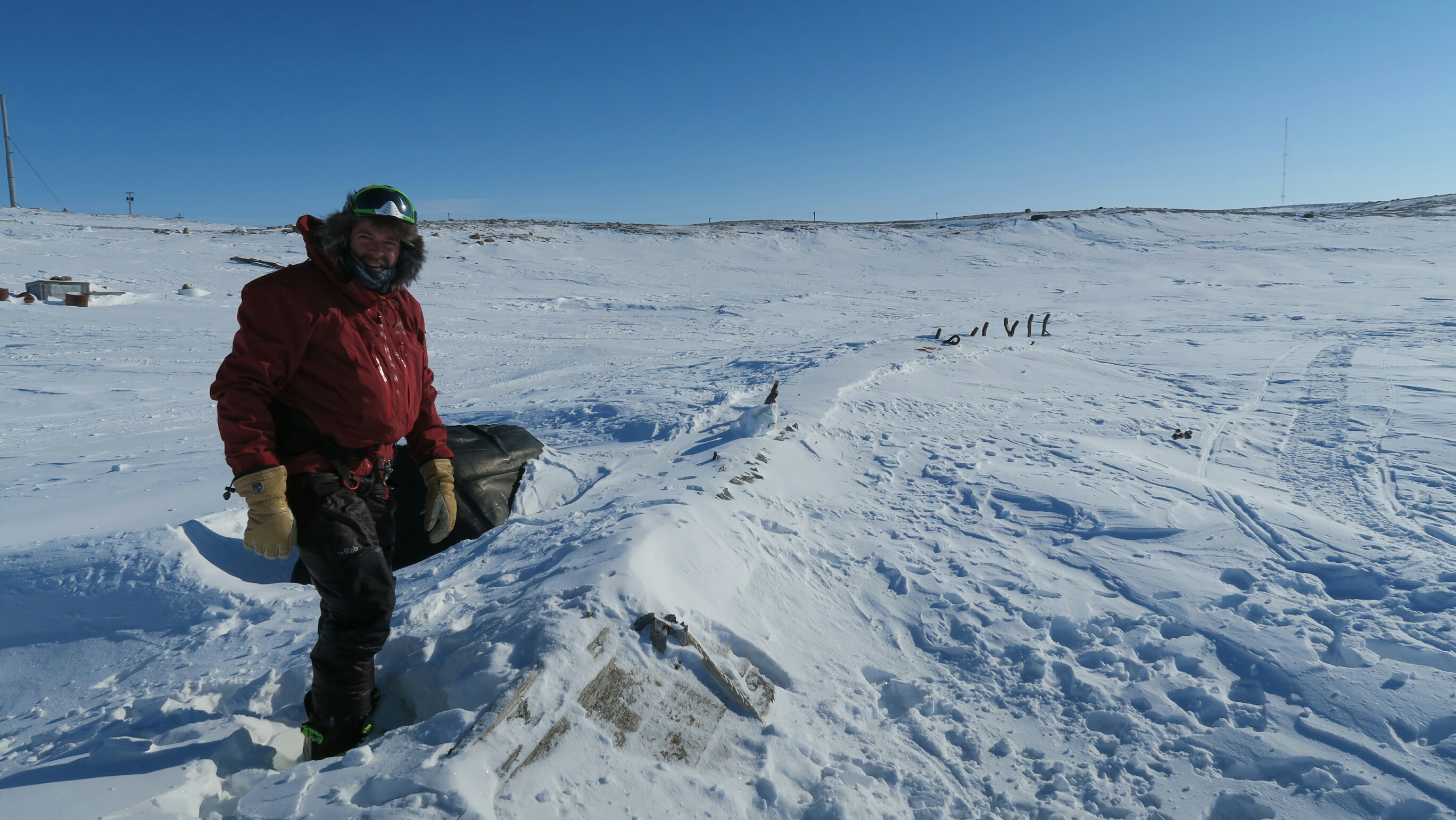 Mann som står ved siden gamle rester av en skute (Maud) som så vidt er synlig under snø.